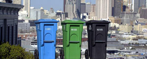 Blue, Green, and Black wheeled cans on top of hill with San Francisco Skyline behind.