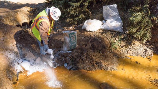 a man in a hard hat sprinkling lime (white power) into a pool of muddy water