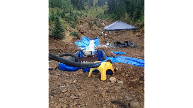 A narrow, forested valley with machinery and pump hoses with a drainage ditch lined with plastic sheets.