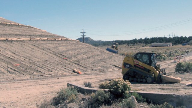 Construction vehicles working on a dusty hillside.