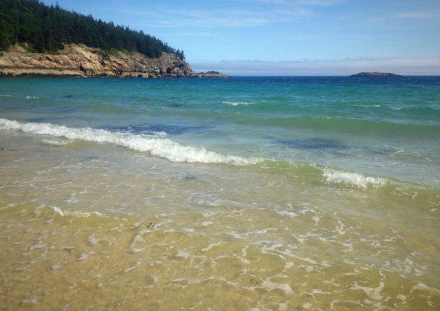 A sandy beach with trees and cliffs in the background