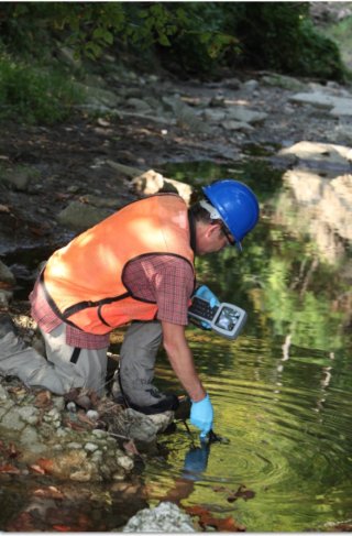 A man near a small river using an electronic device to take water measurements.