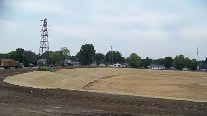 Photograph of a stormwater retention basin at the former quarry pond showing clean fill material. At the outskirt of the image, houses are visible.