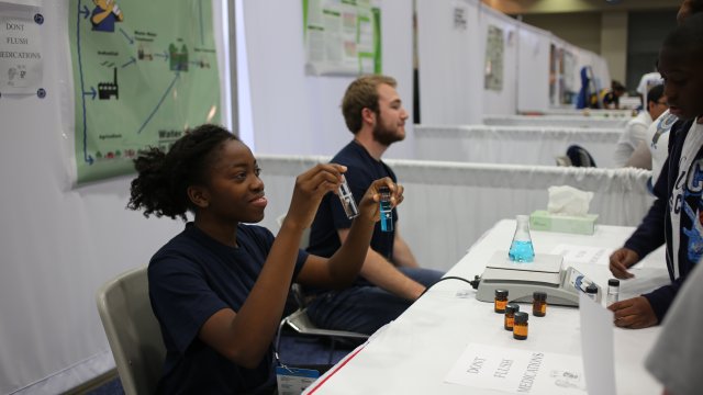 Sideview of two SMU students talking about their project and holding up capped test tubes with colored water