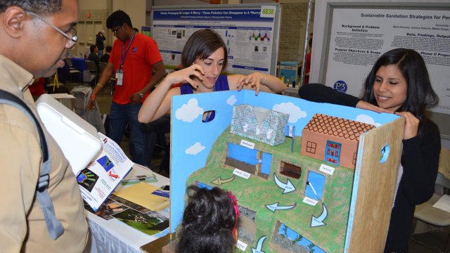 Two University of Rhode Island students presenting a model of their sustainable sanitation strategies project to what appears to be a father and daughter