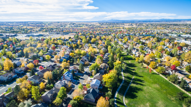 Aerial view of homes with trees and green space with blue sky and clouds in distance