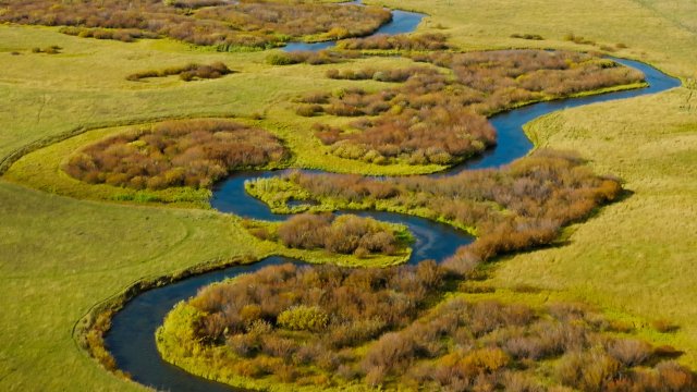 Stream winding through a grassy prairie. 