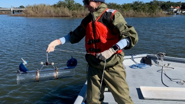 Dr. Jenny Paul in a wetsuit and lifejacket on a fishing boat holding a metal tube.