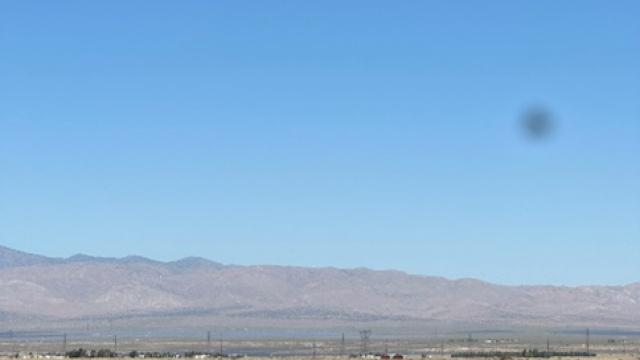 Three people stand in an arid landscape with a drone flying overhead.