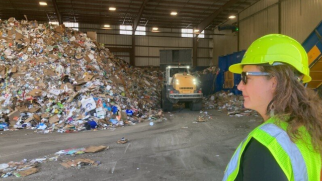 warehouse with paper recycling in a huge pile with Carolyn Hoskinson in a hard hat and a front loader