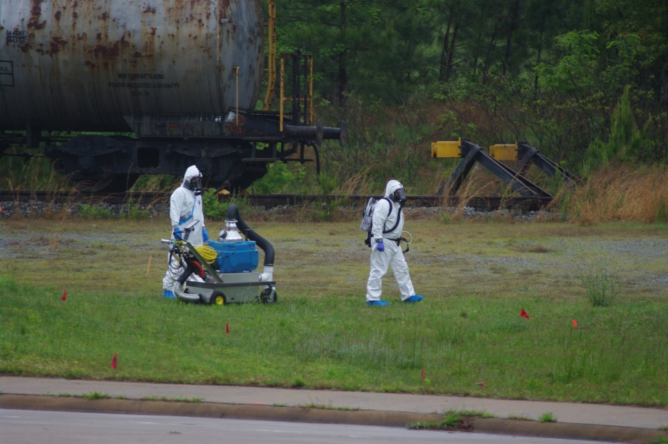 Two team members in tyvek suits walking with the AACeSS mobile system across the grass to take a sample