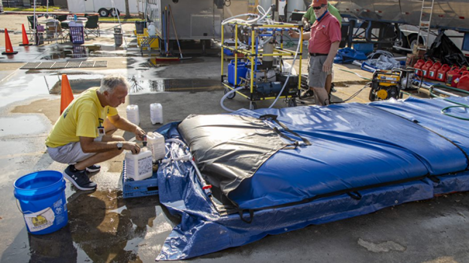 Water treated by the WOW Cart is stored in a blue bladder. A man fills up jugs from the bladder.