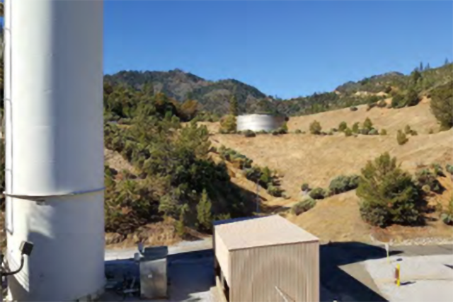 Photograph depicting a mountainous area and an aboveground tank.