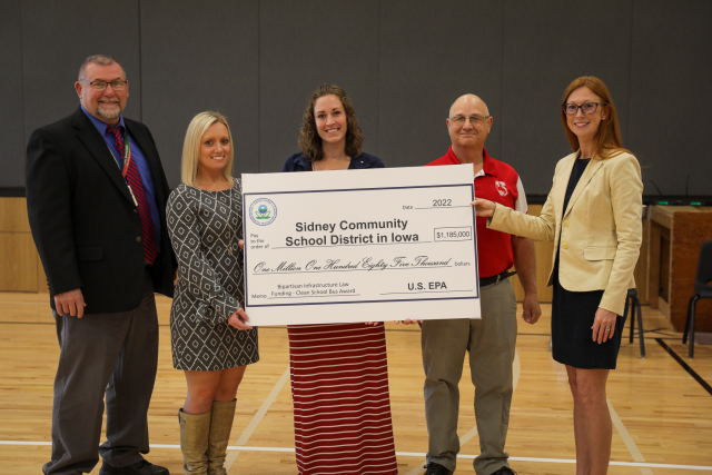 A group stands for a photo next to a large, ceremonial check during a ceremony in a school gym.