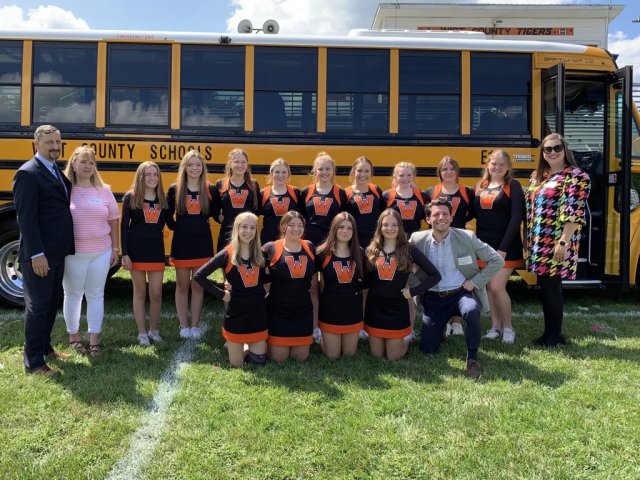 Group of people and cheerleaders standing in front of an electric school bus.