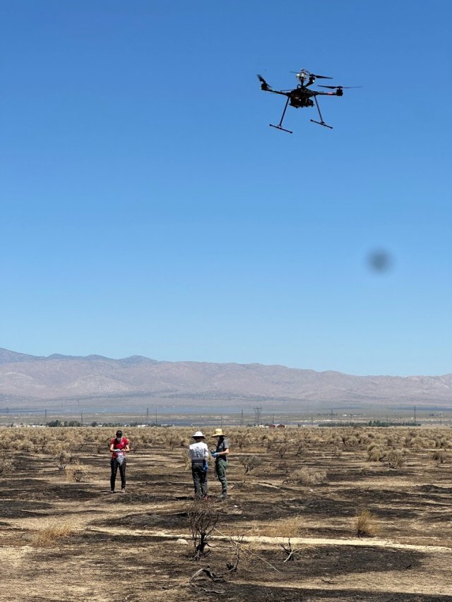 A drone flies above 3 people and a landscape