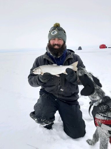 EPA researcher smiling holding a fish while ice fishing on a snowy frozen lake in winter