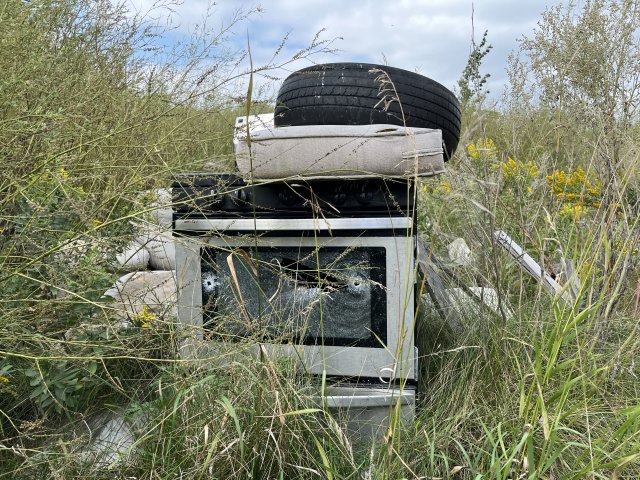 a field with a broken television, a mattress, a tire, and other trash.