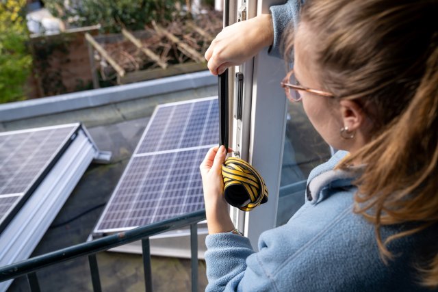 Woman adding weather strips to windows with view of solar panels on roof.