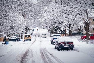 Photo of a snow covered road with car tracks and snow on the trees.