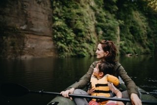 an adult and child sit in a small boat on a calm lake and look at the shoreline in the distance