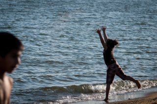 Image of a child throwing sand into the water from shore.