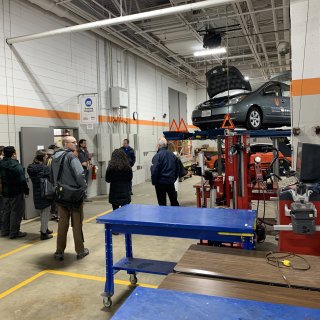 This image shows a group of people touring the Hennepin Technical College's automotive technology facility.