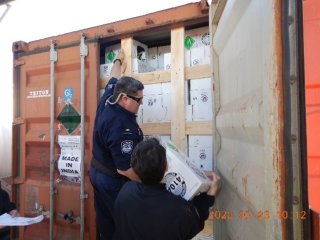 Two federal Customs officers examining boxes labelled 410A, an HFC, in a cargo container at a port.