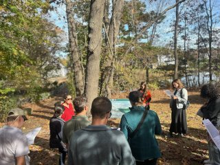 People listen to a presentation in a wooded area.